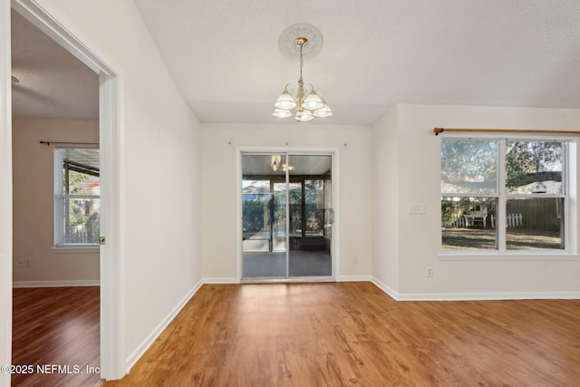 unfurnished dining area featuring a chandelier, a textured ceiling, and hardwood / wood-style flooring