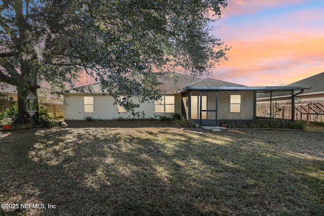 back house at dusk featuring a lawn and a carport