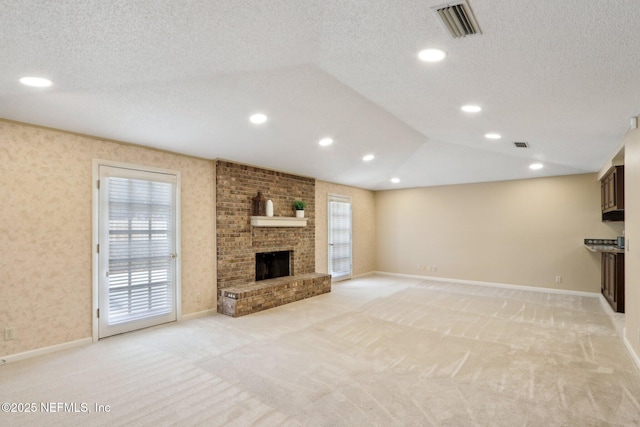 unfurnished living room with lofted ceiling, a brick fireplace, light colored carpet, and a textured ceiling