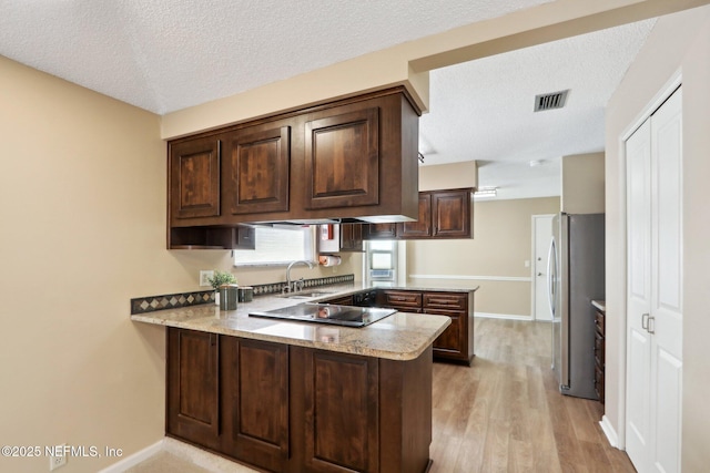 kitchen featuring dark brown cabinetry, stainless steel fridge, kitchen peninsula, and sink