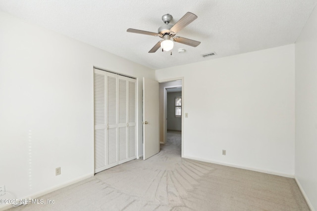 unfurnished bedroom featuring ceiling fan, light colored carpet, a textured ceiling, and a closet