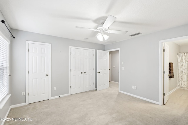 unfurnished bedroom with light carpet, connected bathroom, two closets, and ceiling fan