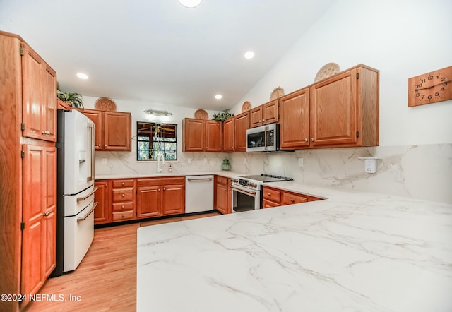 kitchen with sink, light hardwood / wood-style flooring, vaulted ceiling, decorative backsplash, and premium appliances