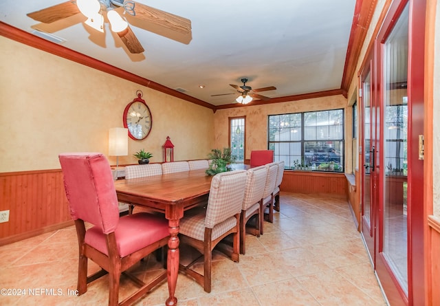 dining area featuring ceiling fan, wood walls, ornamental molding, and light tile patterned floors