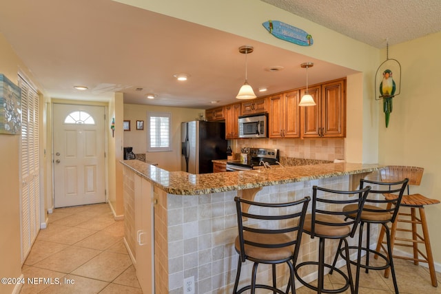 kitchen featuring a kitchen bar, appliances with stainless steel finishes, backsplash, kitchen peninsula, and decorative light fixtures