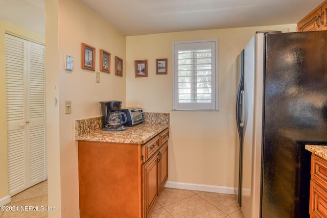 kitchen featuring light tile patterned floors, stainless steel refrigerator, and light stone counters