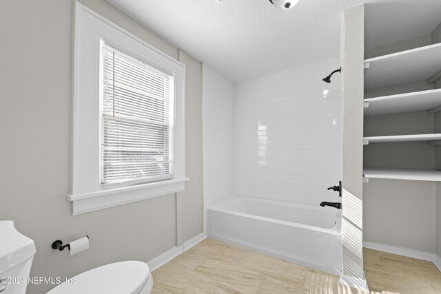 bathroom with a textured ceiling, toilet, tub / shower combination, and a wealth of natural light