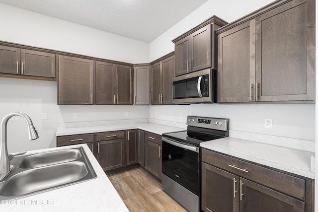 kitchen with dark brown cabinetry, light wood-style flooring, stainless steel appliances, light countertops, and a sink