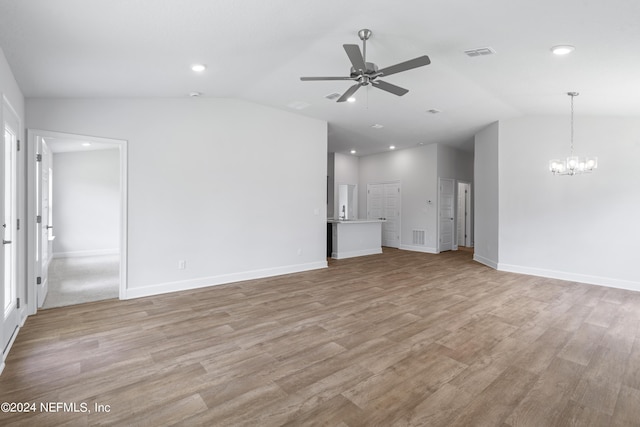 unfurnished living room featuring vaulted ceiling, ceiling fan with notable chandelier, visible vents, and light wood-style floors