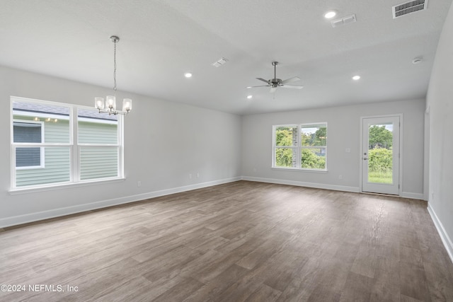 unfurnished room with ceiling fan with notable chandelier, visible vents, baseboards, and wood finished floors