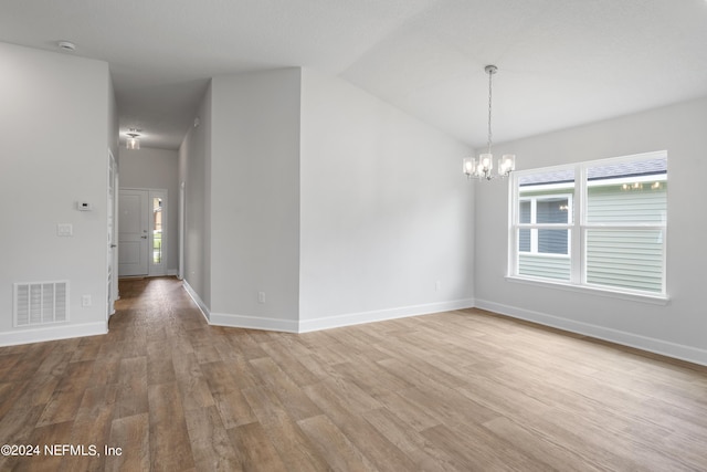 empty room featuring lofted ceiling, visible vents, a notable chandelier, and wood finished floors