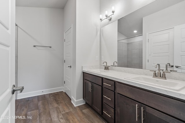 bathroom featuring a tile shower, wood finished floors, a sink, and baseboards