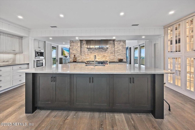 kitchen featuring a large island with sink, white cabinetry, and light stone counters