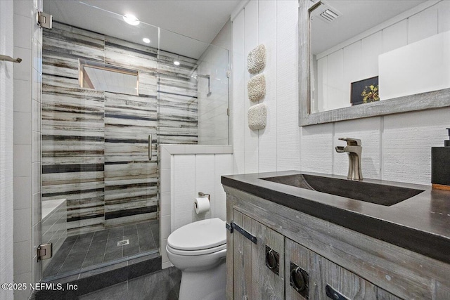 bathroom featuring a shower with door, vanity, tile walls, and toilet