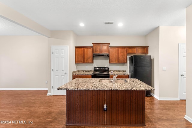 kitchen with sink, light stone counters, dark hardwood / wood-style floors, a center island with sink, and black appliances