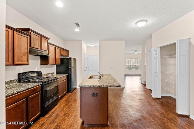 kitchen with dark wood-type flooring, black appliances, a center island with sink, light stone countertops, and a textured ceiling