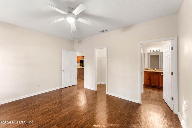 unfurnished bedroom with dark hardwood / wood-style floors, ceiling fan, a spacious closet, connected bathroom, and a closet