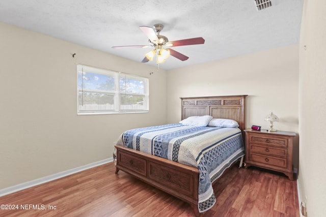 bedroom with ceiling fan, wood-type flooring, and a textured ceiling