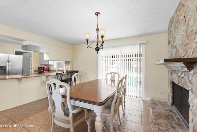 dining room featuring tile patterned flooring, a stone fireplace, a textured ceiling, and a chandelier