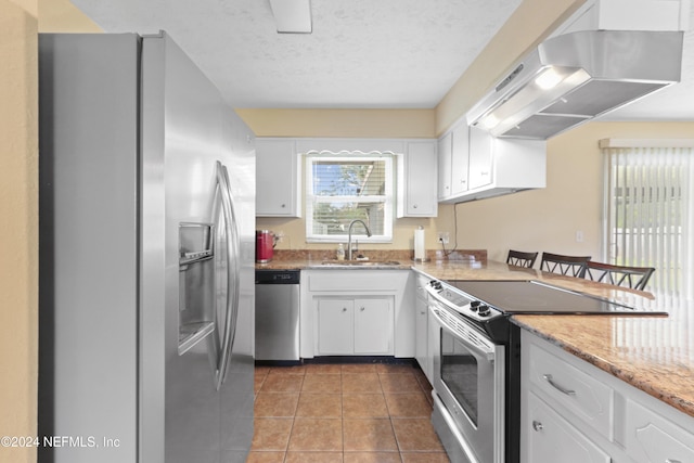 kitchen featuring stainless steel appliances, dark tile patterned floors, sink, exhaust hood, and white cabinetry