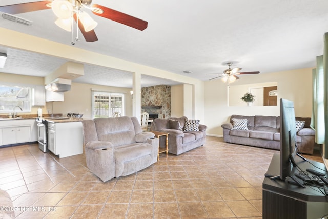 living room with light tile patterned flooring, a textured ceiling, a stone fireplace, and sink