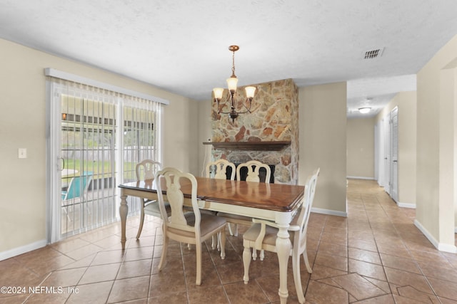 dining area featuring tile patterned flooring, a textured ceiling, a stone fireplace, and a notable chandelier