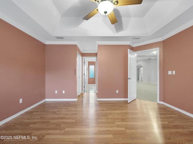 empty room featuring ornamental molding, ceiling fan, a raised ceiling, a textured ceiling, and light hardwood / wood-style flooring