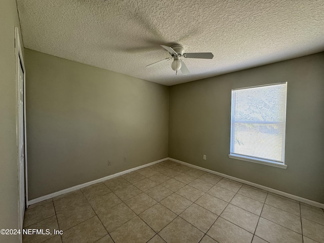 empty room featuring ceiling fan, light tile patterned flooring, and a textured ceiling