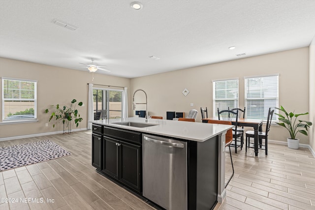 kitchen featuring dishwasher, a kitchen island with sink, sink, light wood-type flooring, and a kitchen bar