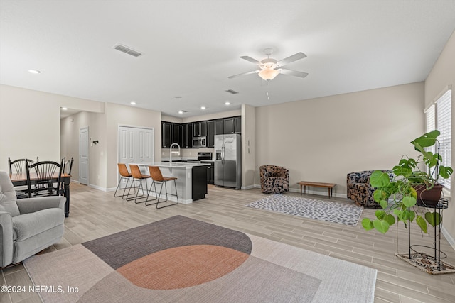 living room featuring light wood-type flooring, ceiling fan, and sink