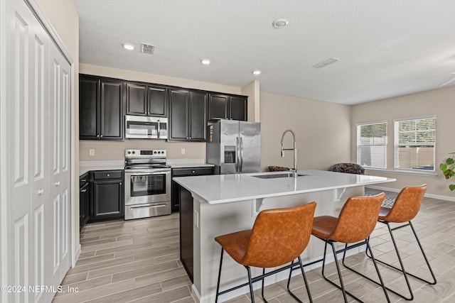 kitchen featuring appliances with stainless steel finishes, light wood-type flooring, sink, a center island with sink, and a breakfast bar area