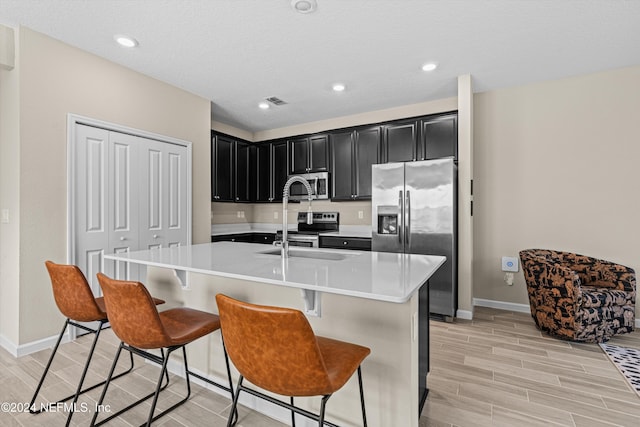 kitchen with a center island with sink, sink, a breakfast bar area, light hardwood / wood-style floors, and stainless steel appliances