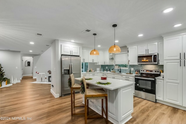 kitchen with stainless steel appliances, a kitchen island, light hardwood / wood-style flooring, a kitchen bar, and white cabinets