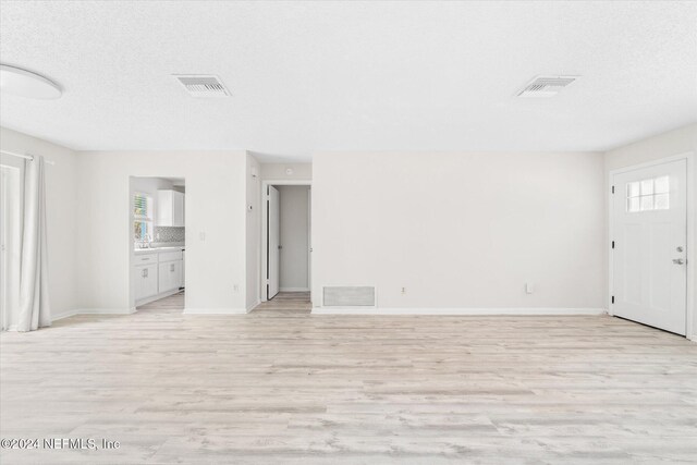 unfurnished living room with light hardwood / wood-style floors and a textured ceiling