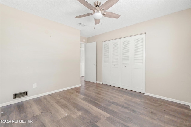 unfurnished bedroom featuring ceiling fan, a closet, wood-type flooring, and a textured ceiling