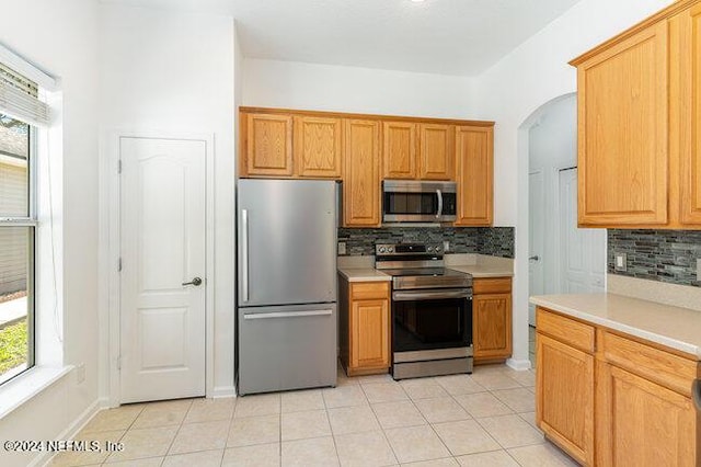 kitchen featuring a wealth of natural light, light tile patterned floors, decorative backsplash, and appliances with stainless steel finishes