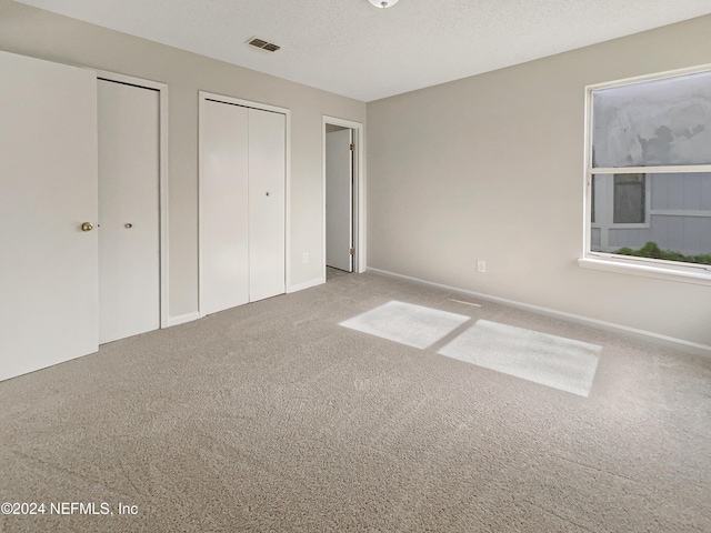 unfurnished bedroom featuring multiple closets, carpet floors, and a textured ceiling