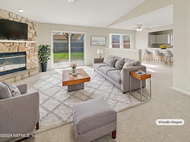 carpeted living room with lofted ceiling, a stone fireplace, ceiling fan, and a textured ceiling