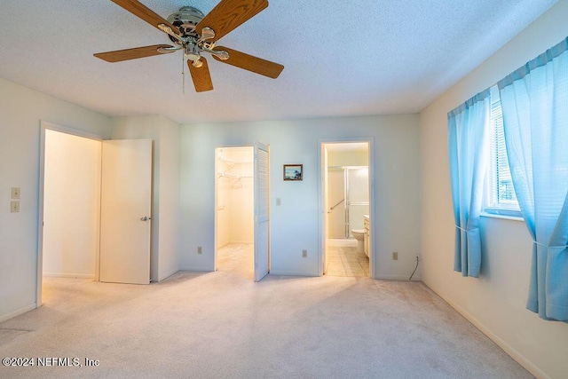 unfurnished bedroom featuring ceiling fan, a spacious closet, ensuite bathroom, light colored carpet, and a closet