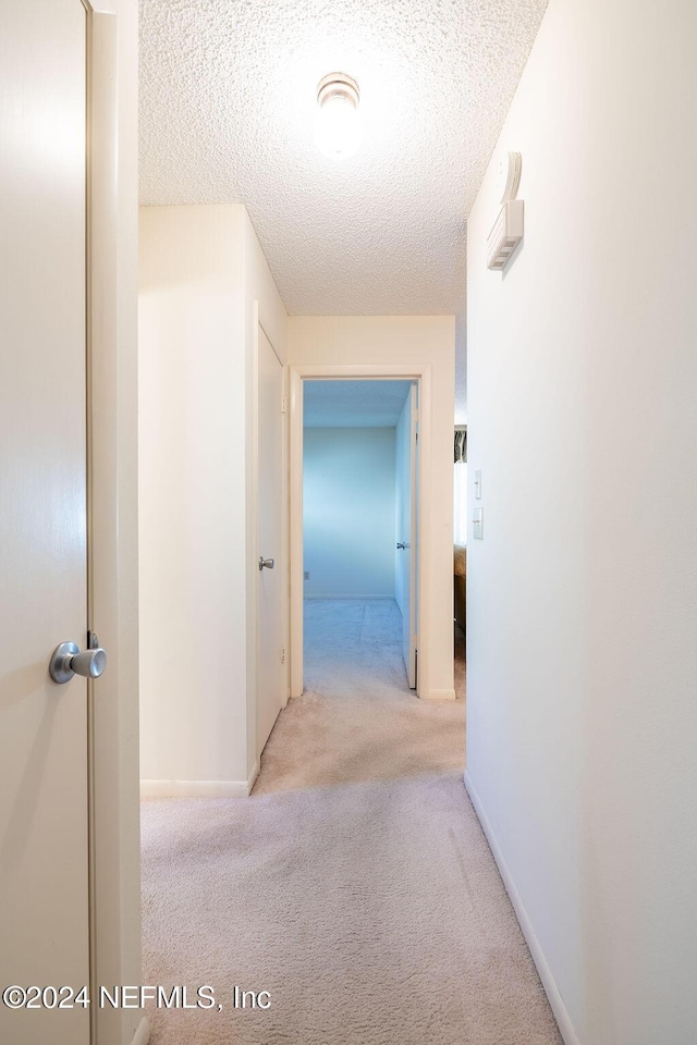 hall with a textured ceiling and light colored carpet