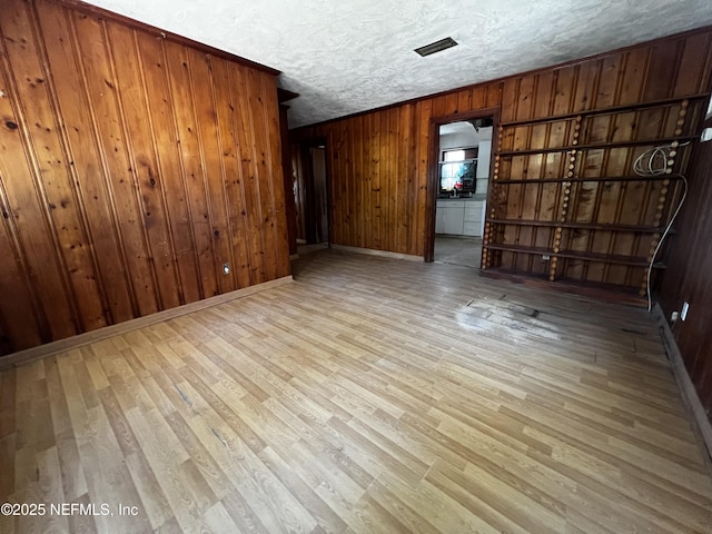 spare room featuring a textured ceiling, light wood finished floors, wood walls, and visible vents