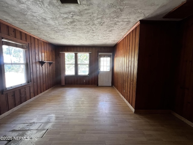 empty room featuring wood walls, wood finished floors, a wealth of natural light, and baseboards