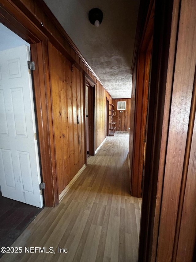 hall featuring a wall unit AC, wooden walls, baseboards, and wood finished floors