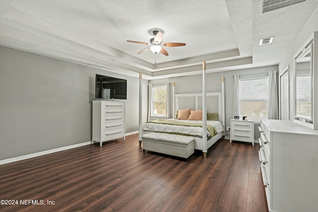 bedroom with a tray ceiling, a textured ceiling, dark hardwood / wood-style floors, and ceiling fan