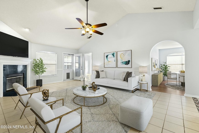 tiled living room featuring ceiling fan, a healthy amount of sunlight, a fireplace, and high vaulted ceiling