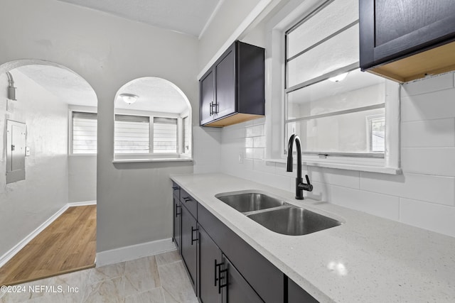 kitchen featuring light stone counters, a textured ceiling, sink, light tile patterned floors, and electric panel