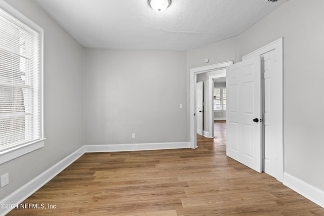 unfurnished room with plenty of natural light, a textured ceiling, and light wood-type flooring