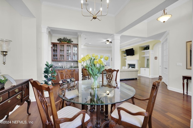 dining area with dark hardwood / wood-style floors, ornate columns, crown molding, and ceiling fan with notable chandelier