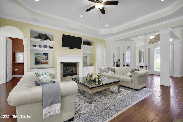 living room featuring a fireplace, ornamental molding, a tray ceiling, and dark wood-type flooring