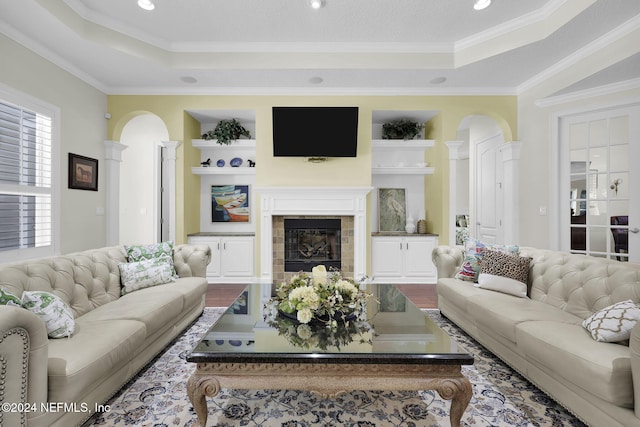 living room with a tile fireplace, wood-type flooring, a raised ceiling, and crown molding